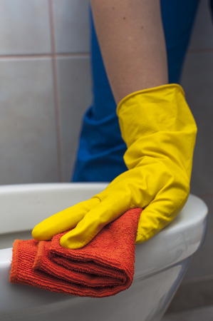 Closeup of woman's hand in yellow glove with rag cleaning the toilet. Housework and cleaning concept.の写真素材