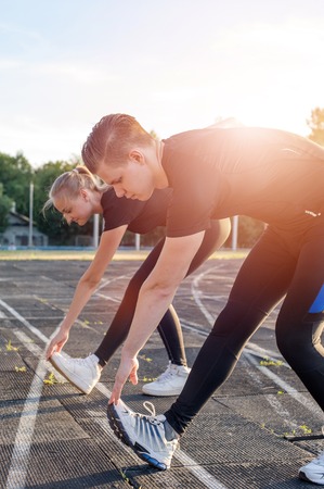 Young cute woman and man stretching their legs before running or fitness workout outdoors.の写真素材