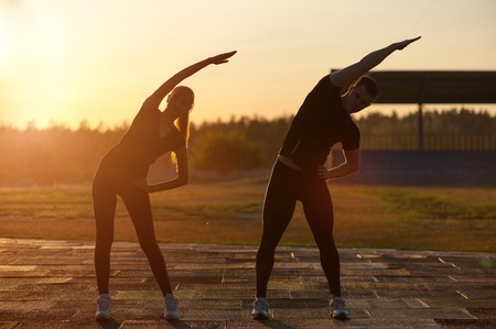 Fitness workout outdoors: young adults doing warming up exercises outdoors at sunset.の写真素材