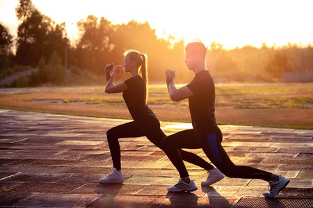 Two silhouettes of fit young man and woman doing lunges outdoors at sunset. Fitness or running workout outdoorsの写真素材