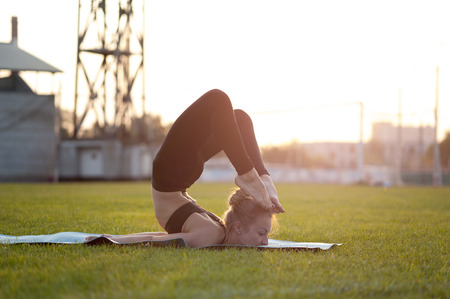 Young flexible woman doing yoga exercises on green grass. Scorpion Pose, Chest Stand, Head to Foot.の写真素材