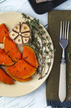 Baked pumpkin with thyme, olive oil and garlic on plate with fork on brown burlap napkin. Vertical view. Vegetarian food.の写真素材