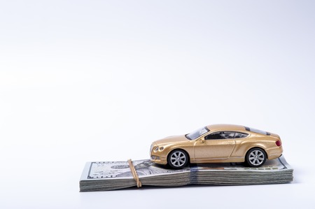 Golden toy car on dollars stack with rubberband on white background.