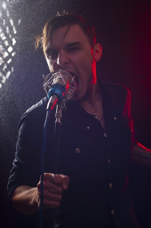 Portrait of young expressive rock singer with microphone at the background of water drops and red spotligts.の写真素材