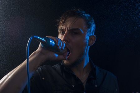 Portrait of young attractive man singing into microphone at the background of spotlights