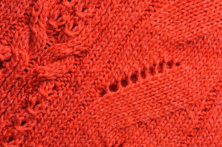 Closeup of knitted ornament on coral woolen texture. Abstract background.
