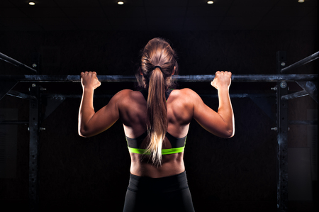 Strong fit girl in sportswear doing pull up exercise on horizontal bar. fitness workout in gym.