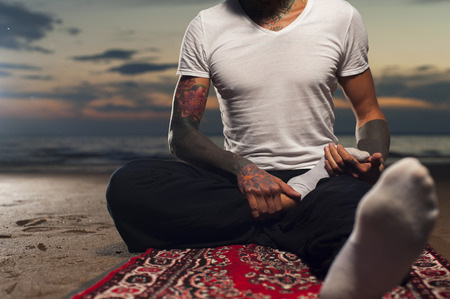 Cropped shot of young man sitting on the beach and doing yoga practice. Lotus position preparing.の写真素材