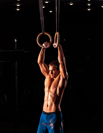 Young muscular man with perfect body doing exercises with gymnastics rings. Fitness, sports concept.
