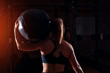 Strong blonde girl holding heavy ball on shoulders.の写真素材