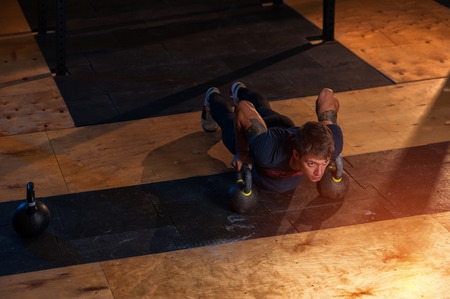 Muscular man doing push ups with kettle bell