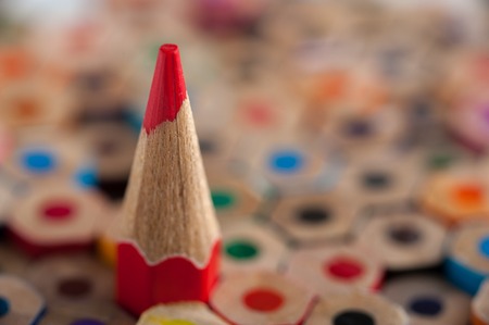 Red sharpened pencil among multicolored crayons