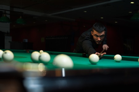 Young handsome man playing billiard game alone