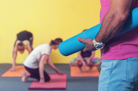 Cropped shot of male adult with exercise mat, females practicing yoga on the background. Body balance training. fitness and healthy lifestyle concept.の写真素材