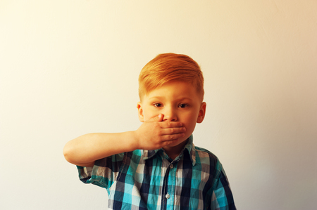 Unhappy child closing his mouth with hands.の写真素材