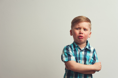 Portrait of angry caucasian child on white background. Unhappy crying boy staying against white wall. Frustration and depression.の写真素材