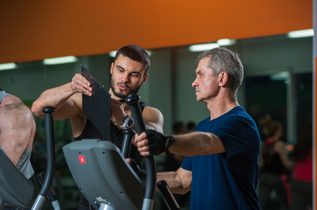 Senior man working with personal trainer in gymの写真素材