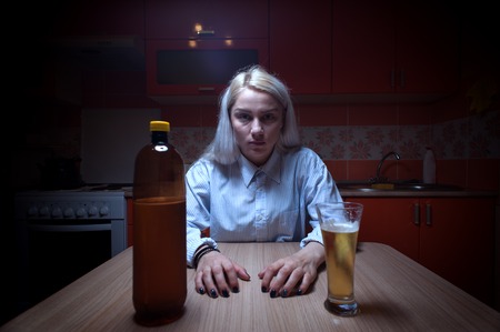 Young woman sitting at the kitchen with beerの写真素材