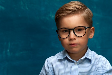 Pensive boy wearing eyeglasses on blue backdropの写真素材