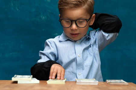 Little stylish boy counting money at workplaceの写真素材