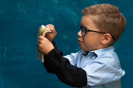 Cute boy sitting at the table and counting moneyの写真素材