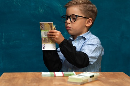 Little stylish boy counting money at workplaceの写真素材