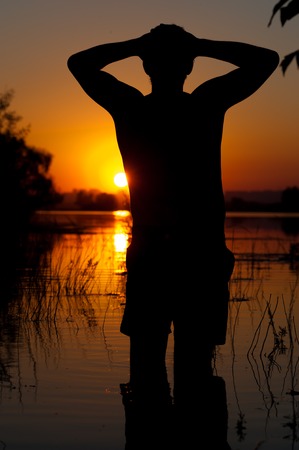 Silhouette of young man watching at river waterの写真素材