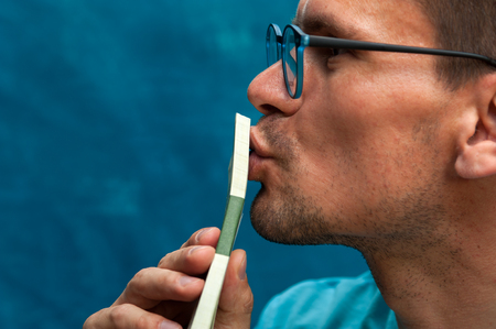 Young man wearing eyeglasses kissing heap of moneyの写真素材