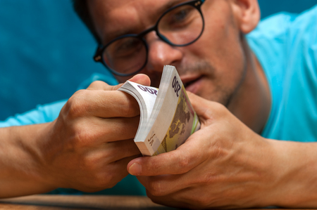 Young stylish man counting heaps of moneyの写真素材