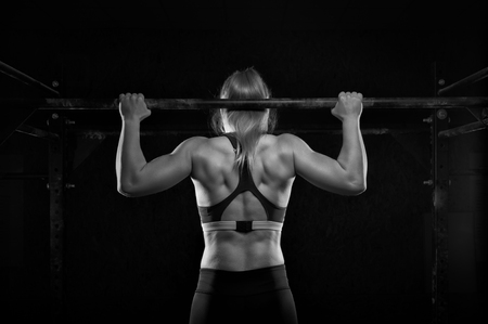 Young muscular woman doing pull up exercise in gymの写真素材