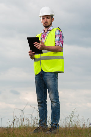 Serious young male chief engineer with a white helmet and green waistcoat signs the project...