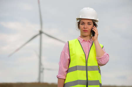 Female chief architect in a green waistcoat holds an smartphone against a background of blurry...