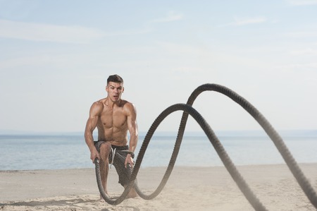 Young man training with battle ropes on the beachの写真素材