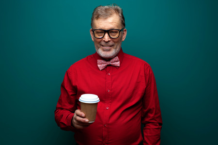Elderly man in red shirt with bow-tie hold coffeeの写真素材