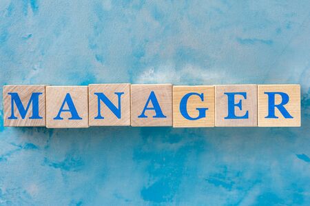 Wooden cubes with word MANAGER on blue table.の写真素材