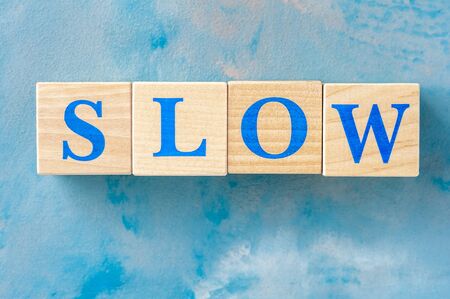 Wooden cubes with word SLOW on blue table.の写真素材