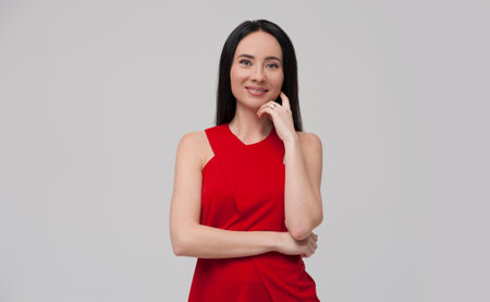 Portrait of charming young brunette woman wearing red blouse posing on grey background.の写真素材