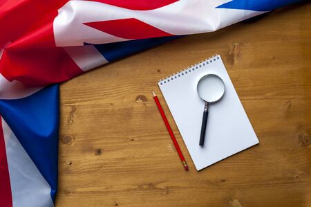 Top view flag of United Kingdom with notepad, pencil and magnifier lie on a wooden table. The concept of finding information and work in the country. Advertising spaceの写真素材
