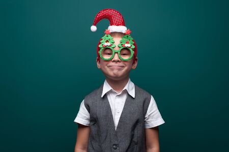 Adorable little boy in Christmas accessories posing on green wallの写真素材