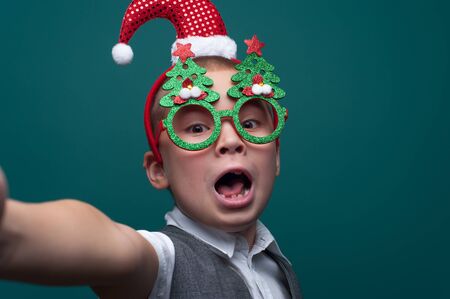 Adorable little boy in Christmas accessories making selfieの写真素材