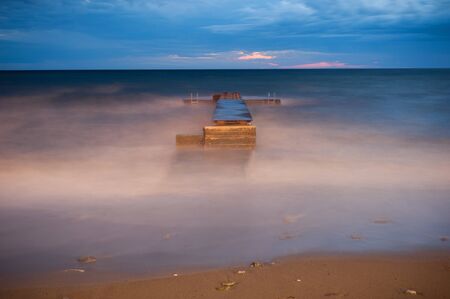 Bewitching view of a wooden bridge located near the shore by the sea in the evening among fog and...