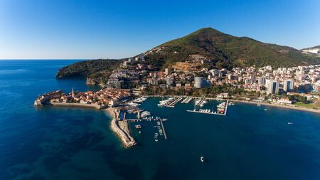 Aerial view of the picturesque coast of Budva in Montenegro with houses and beautiful nature with hills and trees on a sunny warm summer day. Port tourist city conceptの写真素材