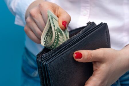 Unidentified woman's hands put rolled paper banknotes in a purse on a blue background. Funds and bank savings accountの写真素材