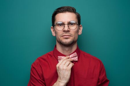 Handsome young man in a red shirt correcting bow-tie against a green backgroundの写真素材