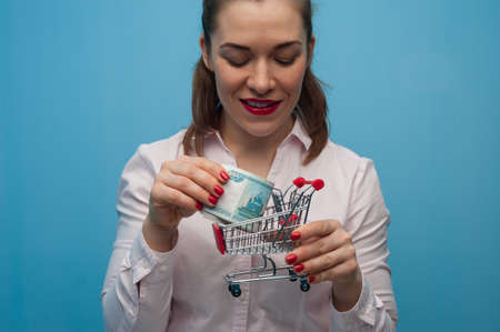 Young woman with a toy grocery basket with a bundle of rubles in her hands.の写真素材