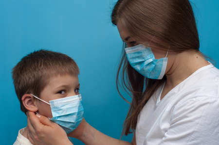 Portrait of caucasian mother and son wearing protective medical mask. Flu epidemic, dust allergy, protection against virus.の写真素材