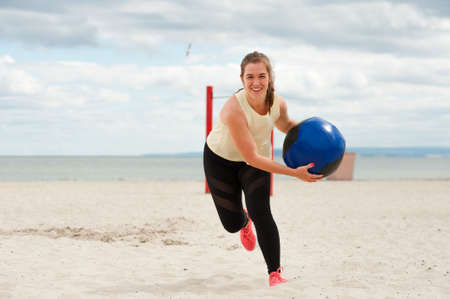 Fit healthy woman wearing sportswear training legs and glutes with heavy ball.の写真素材