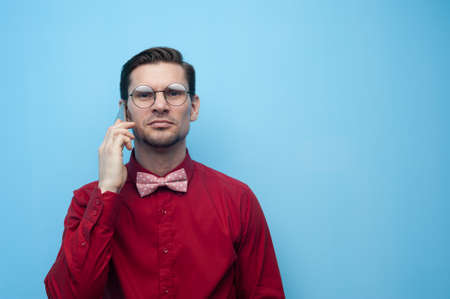 Portrait of a handsome young man in a red shirt and glasses with a smartphoneの写真素材
