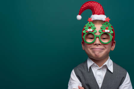Portrait of happy little boy wearing headband with Santa Claus Hat and funny glasses with Christmas treesの写真素材