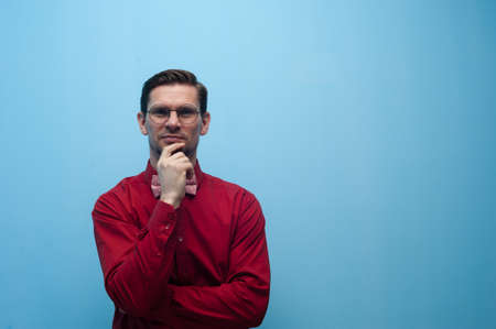 Portrait of thoughtful man in glasses and red shirt posing on blue background.の写真素材